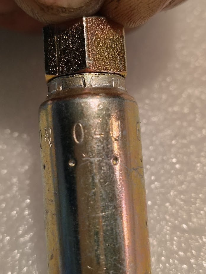 A persons fingers delicately hold a Weatherhead 1/4 Hose x 5/16 JIC/SAE Female Fitting - 45 Swivel (04U-685), showcasing engraved numbers and letters on its hexagonal top against a lightly textured background.