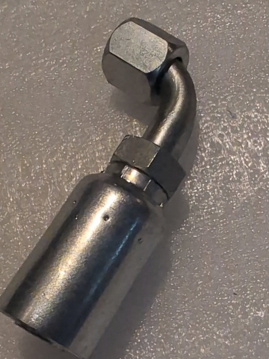 Close-up of a metallic Weatherhead 12U-670 fitting, compatible with 100R17 hoses, featuring a curved design and hexagonal nut, placed on a textured, light-colored surface.