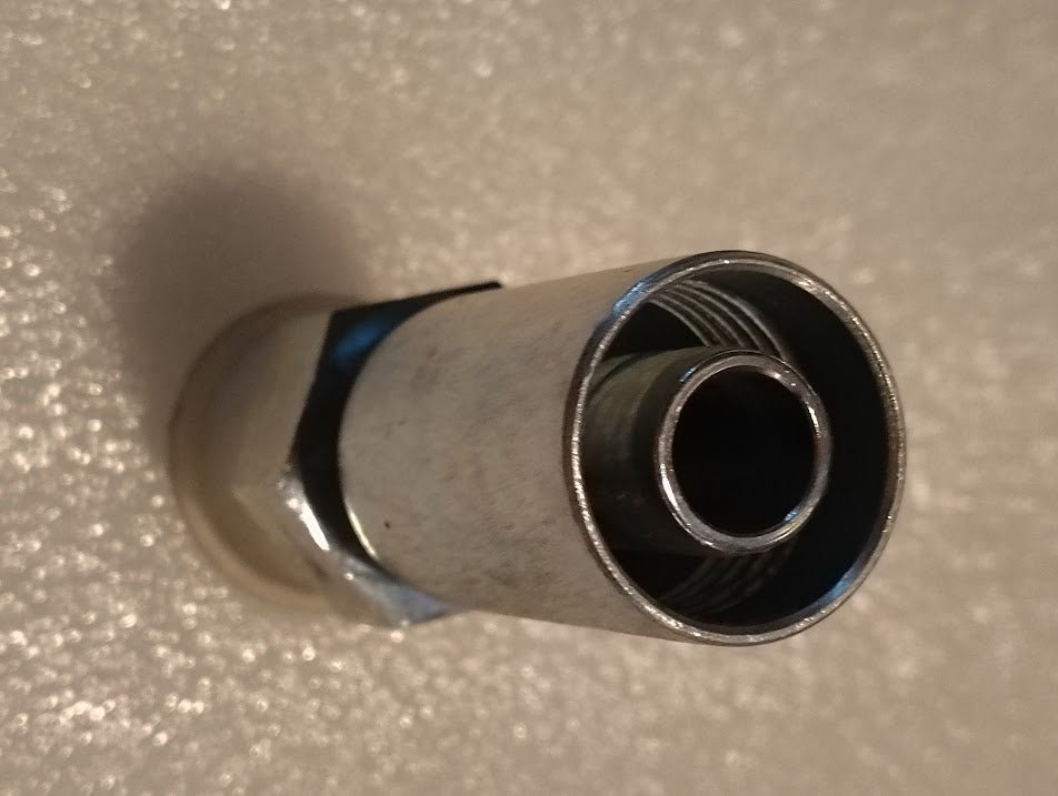 Close-up of a metallic cylindrical 10U-E72 Weatherhead fitting, featuring a shiny threaded interior and hexagonal base, set against a textured light background with partial shadowing.