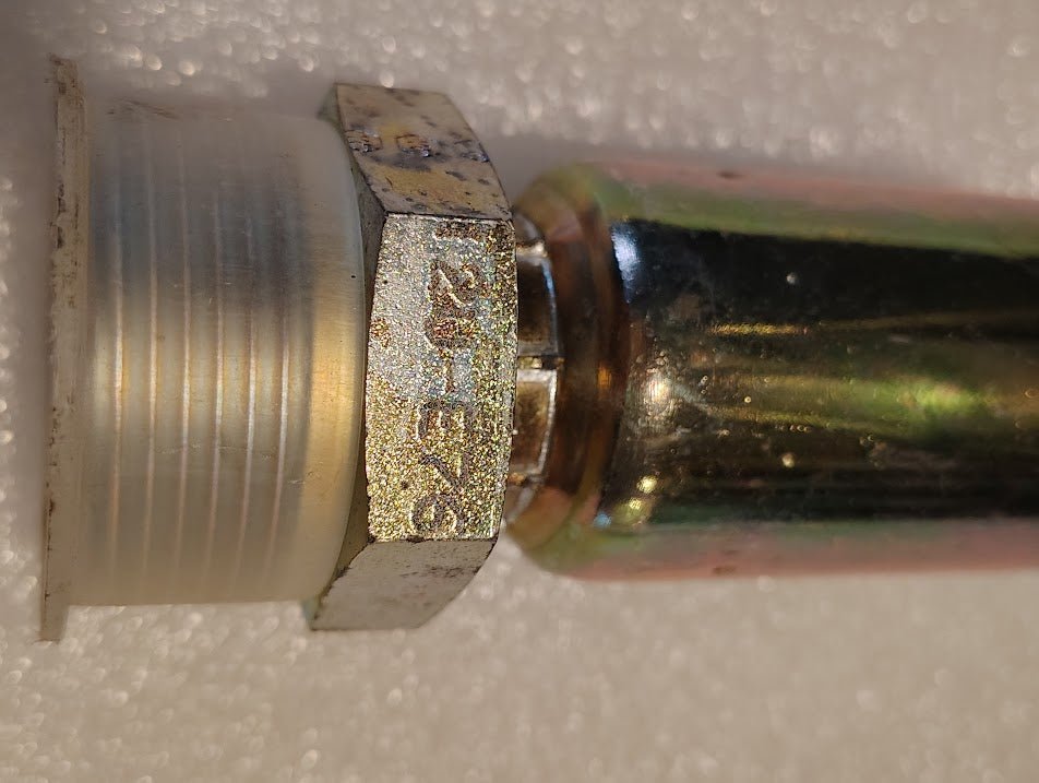 Close-up of a Weatherhead 12U-E76 fitting engraved 28125, attached to a cylindrical pipe against a white background. This metal threaded connector features a hexagonal nut and is designed for hydraulic hoses, compatible with 3/4 hose x 1 ORF male fittings.