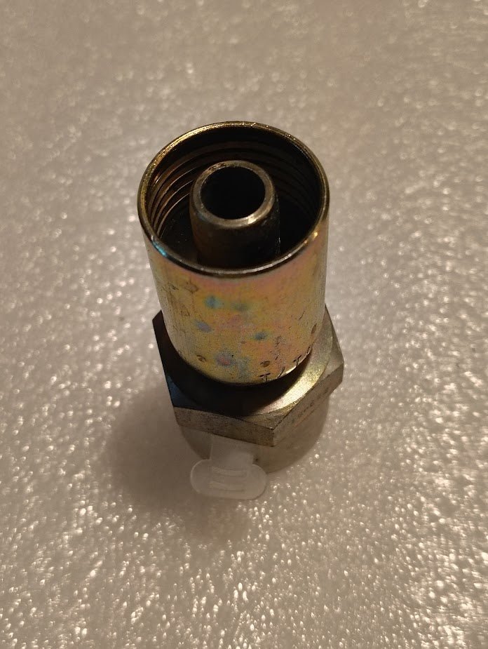 The 08U-E72 Weatherhead fitting integrates a metal pressure sensor on a reflective surface, featuring a threaded top section and hexagonal base, partially obscured by a plastic component, seamlessly with hydraulic hose fittings for improved fluid control.