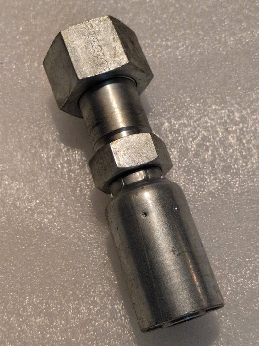 Close-up of a Weatherhead 12U-S76 fitting on a textured surface reveals engineering precision. The shiny, metallic piece features hexagonal nuts and is engineered for 100R1 compatibility, with a 3/4 hose x 1 ORF female straight swivel design.