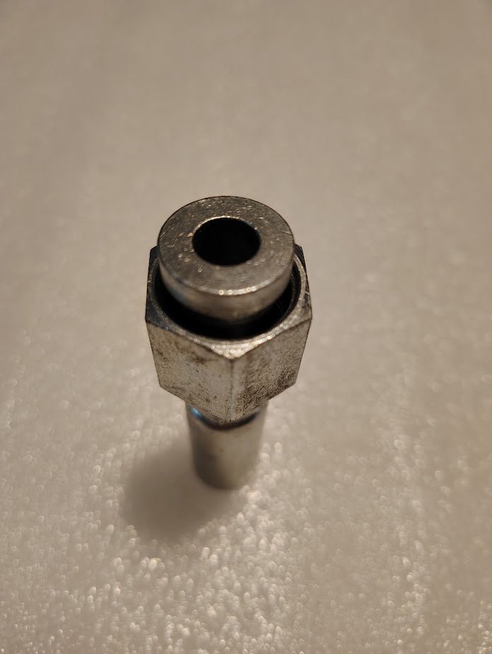 Close-up of a Weatherhead 04U-S68 fitting, standing on a textured white surface. The circular opening at the top shows slight wear and oxidation, while the lighting highlights its metallic texture and surface details.