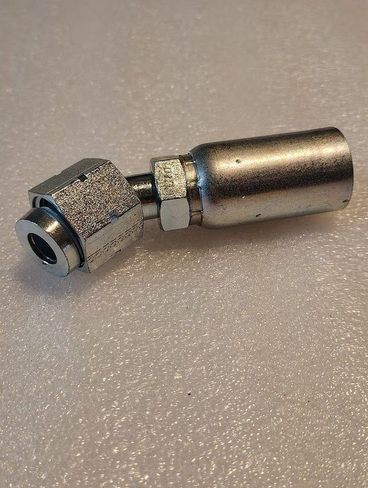 A close-up of the 10U-L70 Weatherhead fitting, featuring a hexagonal nut and cylindrical body, lies on a textured white surface. This shiny 5/8 hose x 5/8 ORF female fitting with a 45 swivel is perfect for effortlessly connecting compatible hoses or pipes.