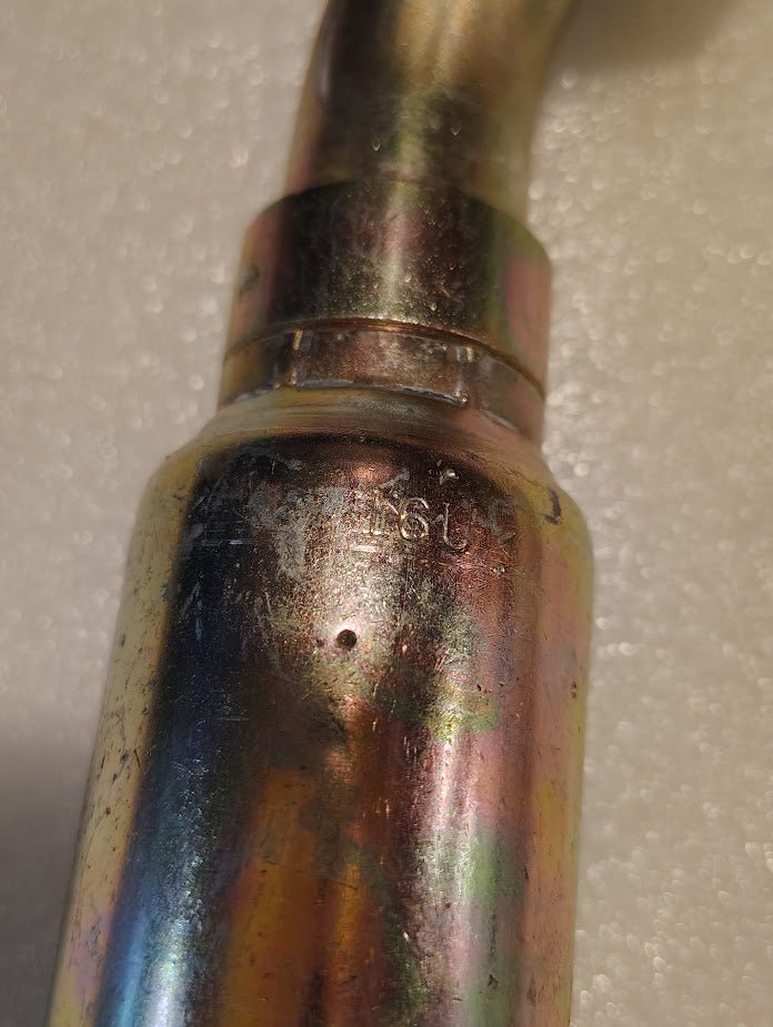 Close-up of the 16U-L76 Weatherhead 1 Hose x 1 ORF Female Fitting - 45 Swivel, showcasing its metallic pipe with a reflective, multicolored surface on a textured white background. The flared joint resembles hydraulic hose fittings with engraved numbers and slight wear on the surface.