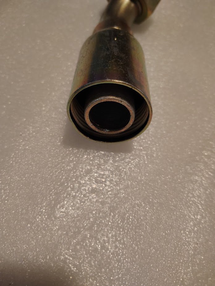 Close-up of a 16U-L76 Weatherhead 1 Hose x 1 ORF Female Fitting - 45 Swivel, a metal cylinder with a threaded interior, on a textured white surface.