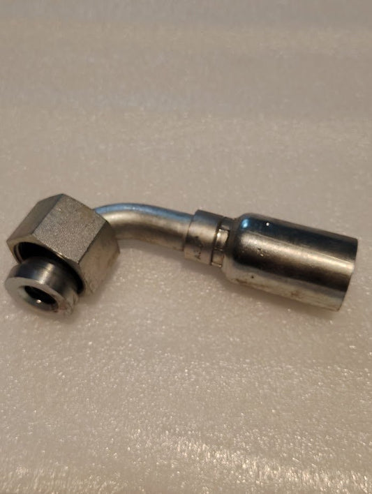 A Weatherhead 12U-A36 fitting, designed for 3/4 hoses and featuring a 1 ORF female connection with a short swivel elbow, lies on a textured light gray surface. The hydraulic fitting includes a hexagonal nut and cylindrical connector.
