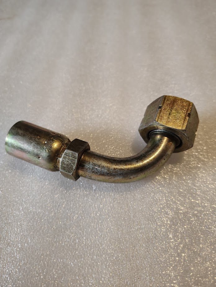 A 90-degree Weatherhead fitting (08U-A32) lies on a textured surface, featuring a shiny cylindrical end and hexagonal nut, ideal for plumbing or mechanical use.
