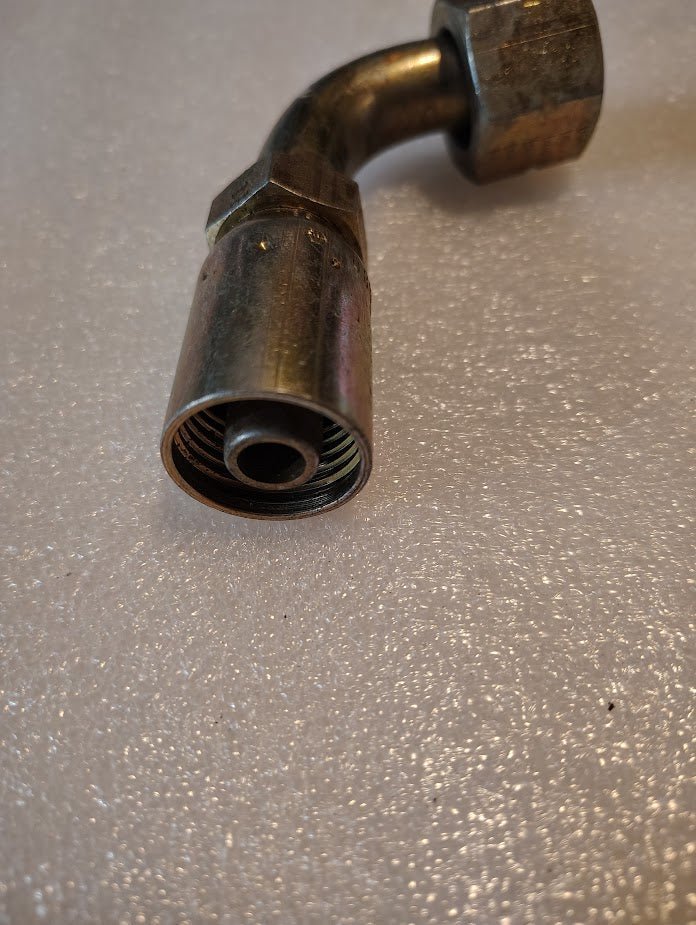 Close-up of a 08U-A32 Weatherhead 1/2 hose x 3/4 ORF female fitting - 90 short swivel, featuring a threaded end and hexagonal nut on a textured, light-colored surface.