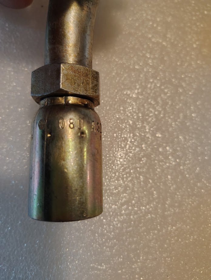 A close-up of the 08U-A32 Weatherhead fitting, featuring a threaded connection and curved pipe, perfect for 100R1 hoses. The surface shows engraved numbers against a textured white background.