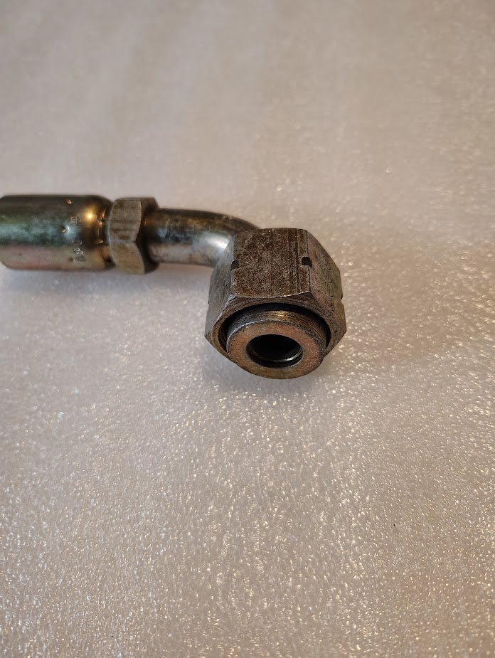 A close-up of the 08U-A32 Weatherhead fitting, featuring a 1/2 hose x 3/4 ORF female end with a 90-degree short swivel, rests on a textured light surface. The cylindrical metal shows slight wear and patina, while the hexagonal nut ensures secure tightening.