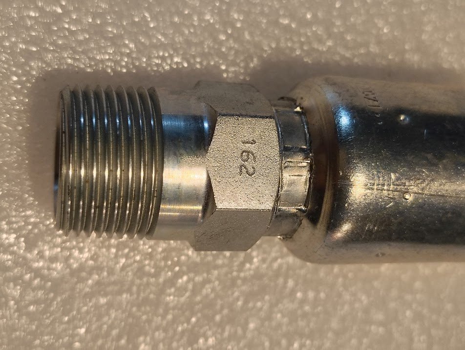 Close-up of a metallic 12U-162 Weatherhead 3/4 Hose x BSPT Male Fitting with 162 engraved on it, set against a textured white background.