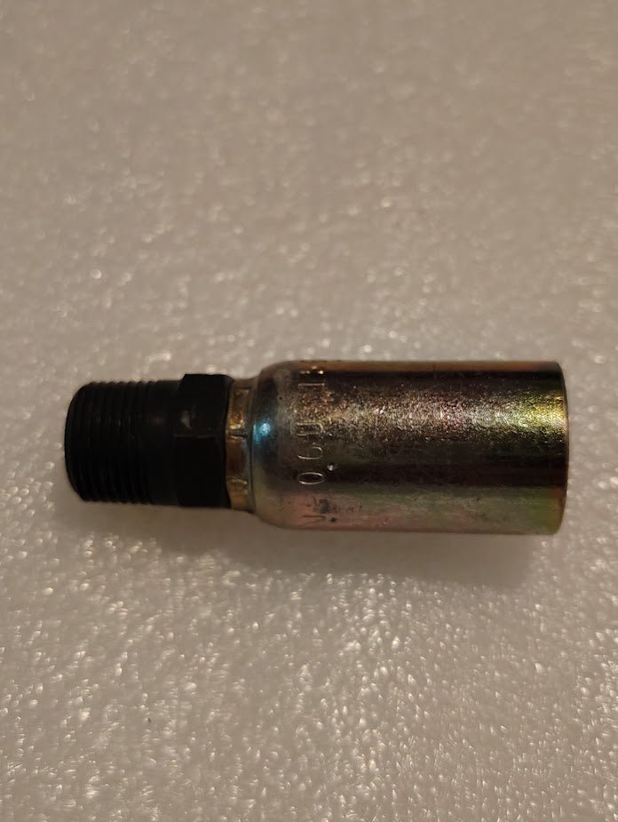 A metallic 06U-156 Weatherhead 3/8 Hose x 3/8 BSPT Male Fitting, with a threaded black end, rests on a textured white surface. Slightly worn and discolored, it resembles fittings commonly used in hydraulic systems.