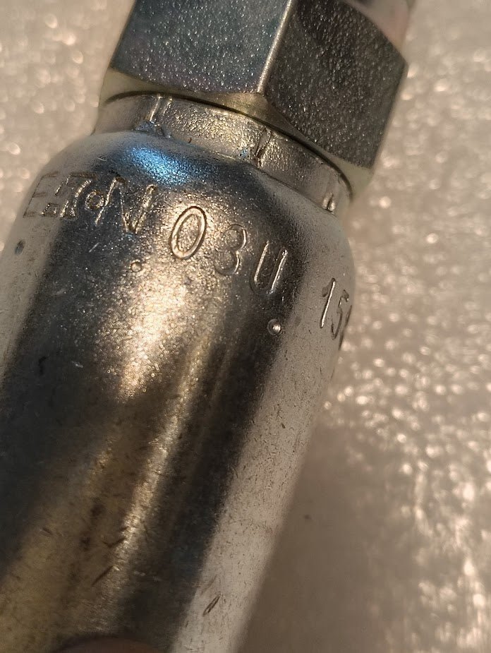 A close-up of a metallic spark plug engraved with 03U evokes the precision of the Weatherhead 08U-158 hose fitting. The shiny finish reflects light beautifully against a textured white backdrop, reminiscent of intricate hydraulic parts.