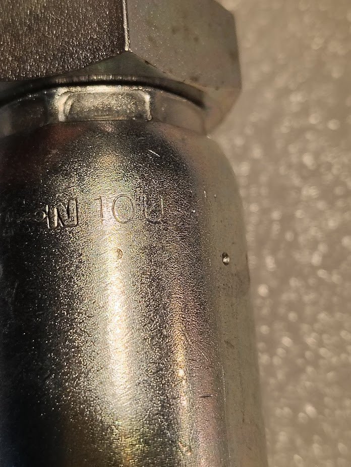 A close-up of a metallic cylindrical object shows an engraved 10U on the shiny surface, reflecting light against a textured background, reminiscent of the accuracy in the 10U-P60 | Weatherhead 5/8 Hose x 5/8 BSPT Male Fitting - Straight Solid.