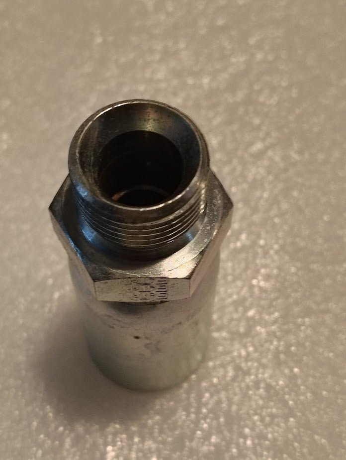 A 10U-P60 Weatherhead 5/8 Hose x 5/8 BSPT Male Fitting, featuring a cylindrical shape with a hexagonal middle and interior threading, is shown close-up on a textured, light-colored surface—ideal for compatible hoses.