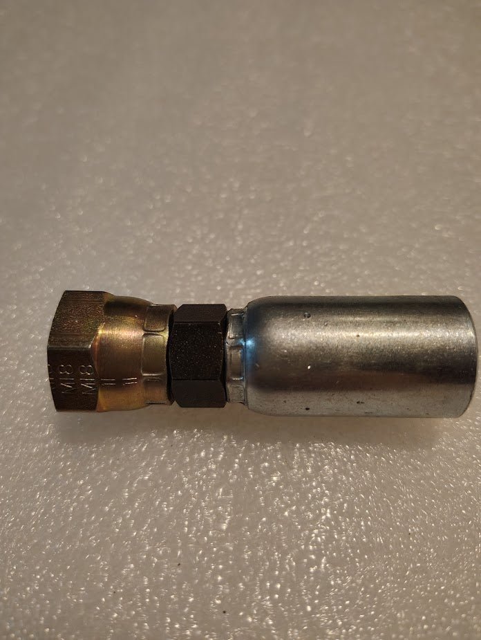 The Weatherhead 06U-12C fitting, featuring a brass-colored hexagonal nut and cylindrical silver end, is crimped onto a metal hydraulic hose and placed on a textured white surface.
