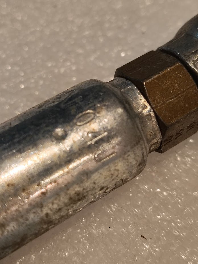 A close-up shows a metallic pipe with a Weatherhead 04U-58C Brass Hexagonal Fitting, 1/4 Hose to M16x1.5 DIN Female Straight Swivel. The surface has slight weathering similar to hydraulic hose markings, set against a textured white background.
