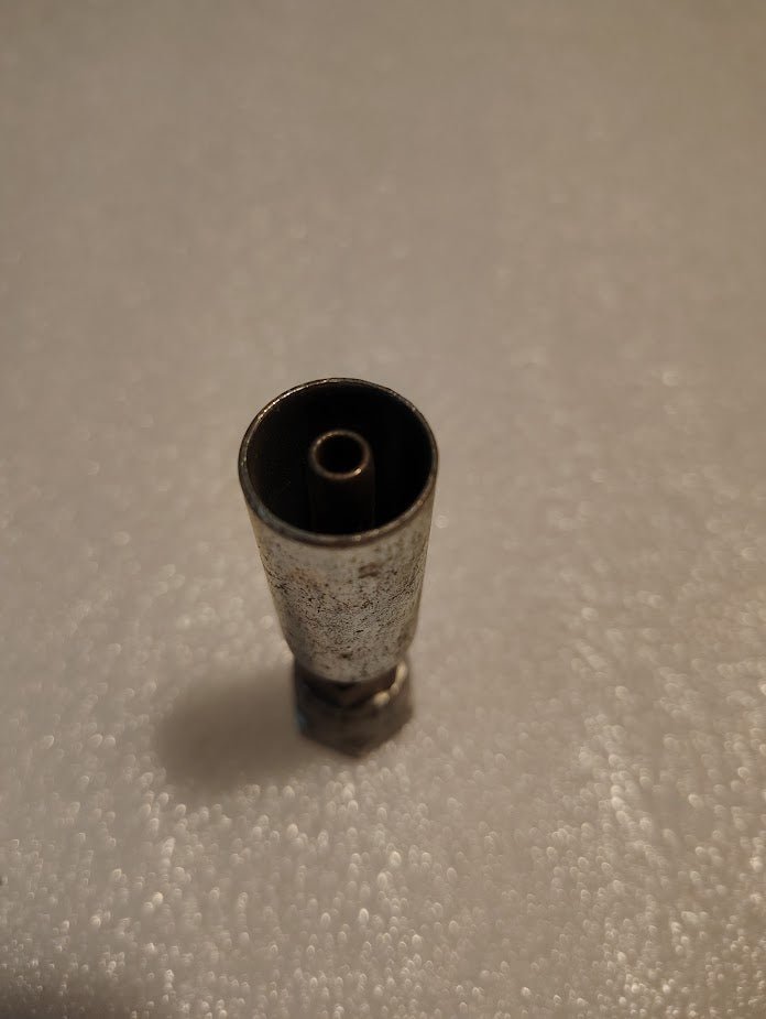 A close-up of the 04U-58C Weatherhead 1/4 Hose x M16x1.5 DIN Female Fitting - Straight Swivel, resembling a small metallic cylinder with a textured surface. It stands upright on a speckled light background, featuring a hollow center with an inner cylinder.