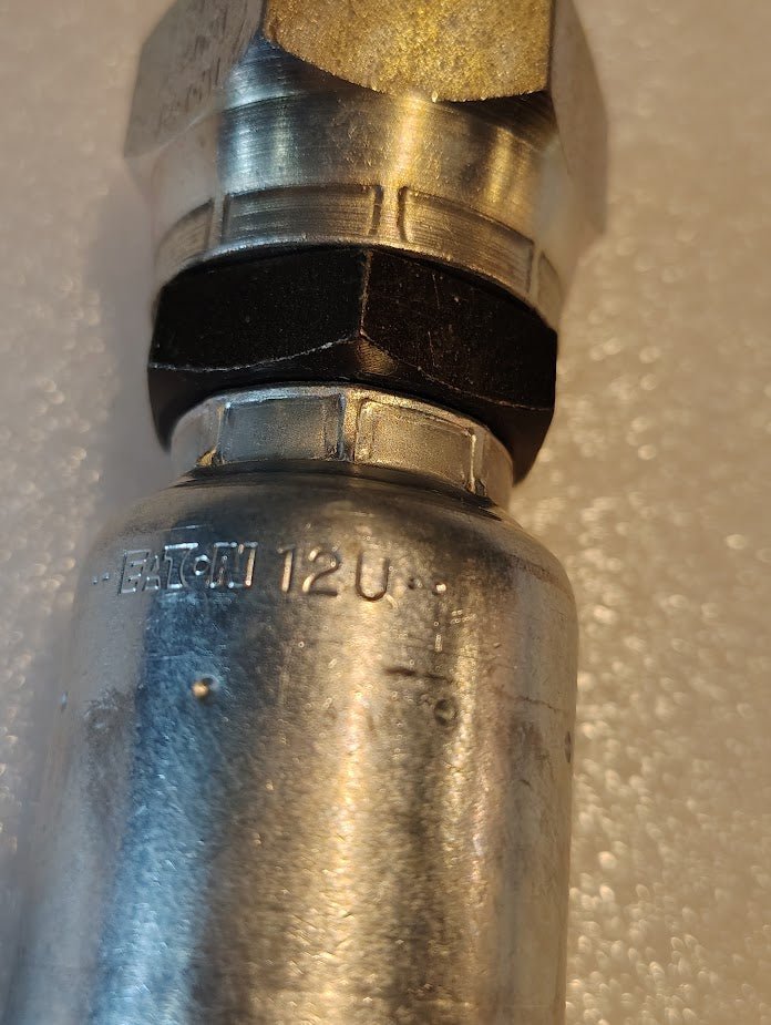 A close-up of a metal fitting engraved EATON 12U highlights the quality of Weatherheads 12U-30K fittings. This 3/4 Hose x M30x1.5 Komatsu Female Fitting features a two-toned design with a silver finish and black section against a light background.
