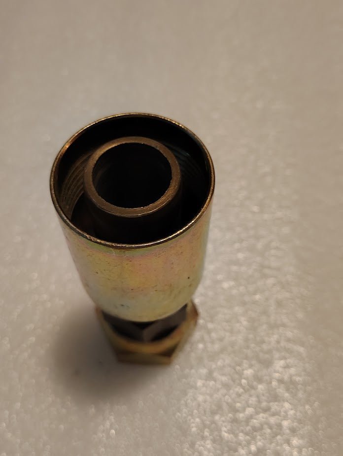 A close-up of a shiny, metallic 16U-33K Weatherhead 1 Hose x M33x1.5 Komatsu Female Straight Swivel Fitting with visible threading, compatible with Weatherhead fittings, resting on a textured white surface.