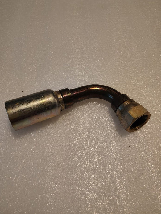 The 12U-82P, a metallic Weatherhead fitting with silver and bronze tones, features a threaded nut on one end and cylindrical connector on the other for 100R1 hoses. It rests slightly tarnished on a textured, light surface.