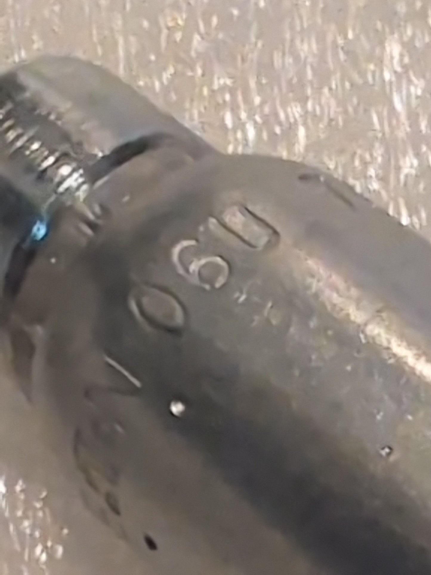 A close-up of a 06U-76P Weatherhead fitting reveals engraved numbers like 090 on its slightly worn surface, against a textured background, suggesting its use in hydraulic hose assemblies.
