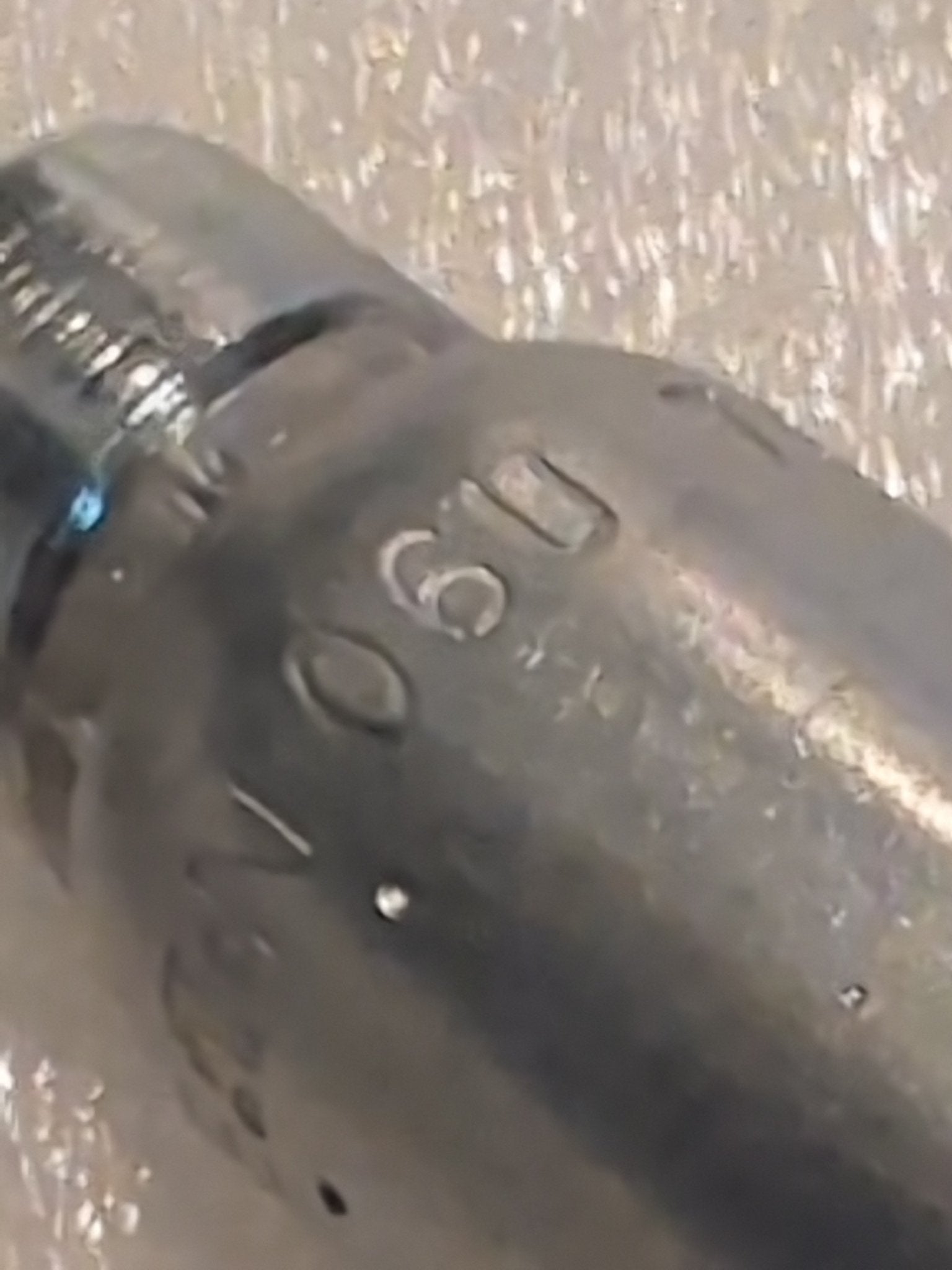 A close-up of a 06U-76P Weatherhead fitting reveals engraved numbers like 090 on its slightly worn surface, against a textured background, suggesting its use in hydraulic hose assemblies.