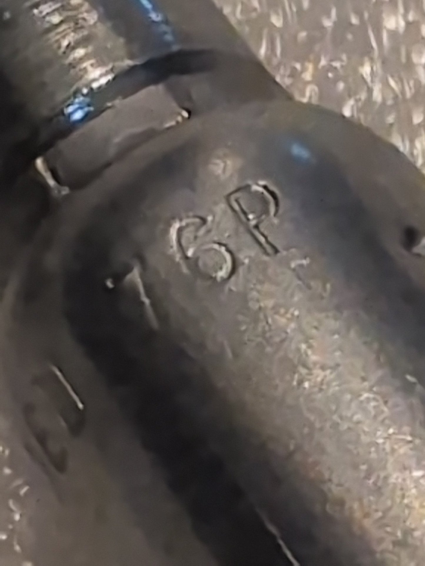 Close-up of a metallic object with 76P engraved on its textured, dark surface. The cylindrical shape resembles the 06U-76P Weatherhead 3/8 Hose x 3/8 BSPP Female Fitting - 90 Swivel, highlighted against a blurred backdrop emphasizing engraving precision.