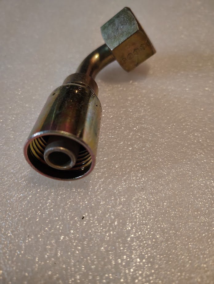 A close-up of a Weatherhead 08U-80P fitting, featuring a 1/2 hose to 5/8 BSPP female connection with a 90-degree swivel and internal threading. Its positioned diagonally on a textured, light gray surface, resembling Parker fittings with curved pipe and hexagonal nut design.