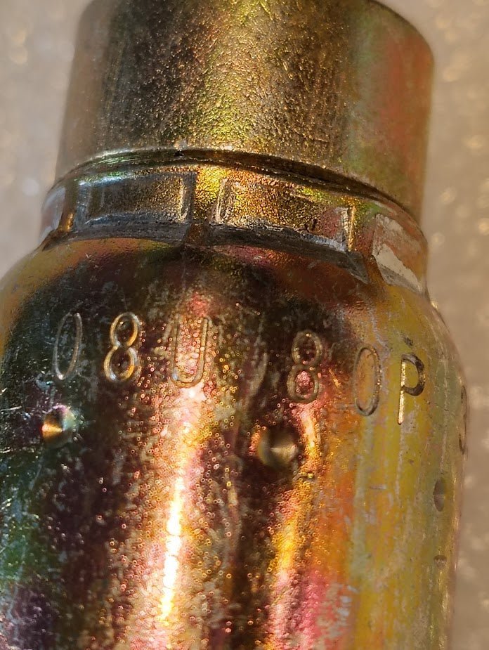 The image shows a close-up of the metallic Weatherhead 08U-80P fitting, resembling hydraulic hose parts, with 08U80P engraved. It has an iridescent surface reflecting gold, green, and orange hues against a softly blurred backdrop.