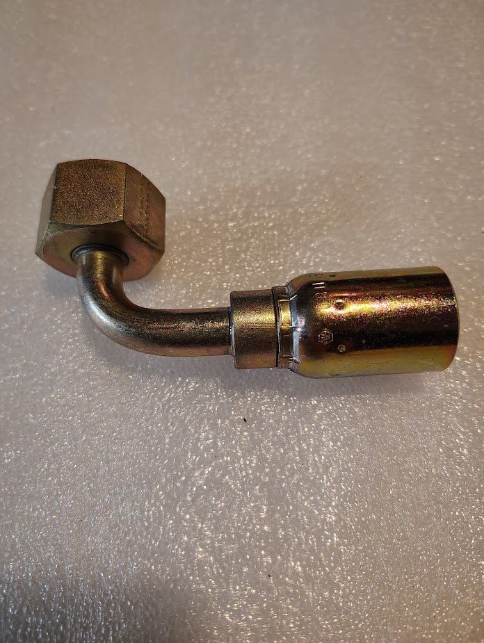 The 08U-80P, a Weatherhead 1/2 Hose x 5/8 BSPP Female Fitting with a smooth cylindrical end and hexagonal nut, features a shiny finish and precise 90-degree swivel. It rests on a textured white surface, compatible with 100R1 hoses.