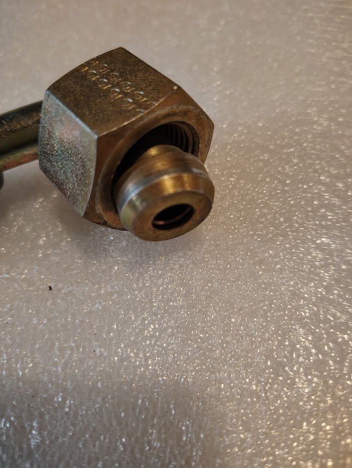 A 90-degree swivel nut, reminiscent of Parker fittings, is attached to a threaded pipe. The metallic Weatherhead 08U-80P 1/2 hose x 5/8 BSPP female fitting rests on a textured, light surface showing slight wear and tarnish.